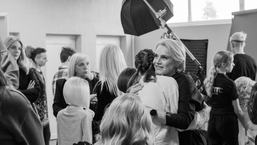 Black and white photo of people hugging and smiling backstage at a fashion event.